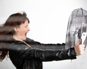 woman suffering from hot flashes holding fan in front of face